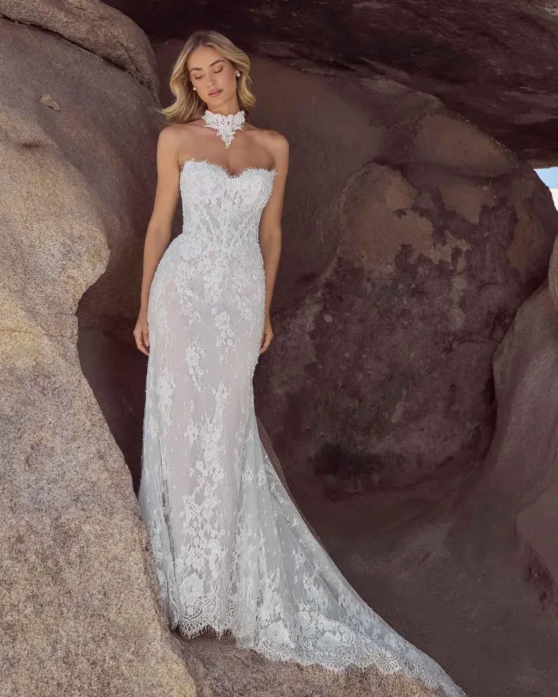 A woman in a beautiful strapless lace wedding gown stands gracefully against a rocky backdrop.