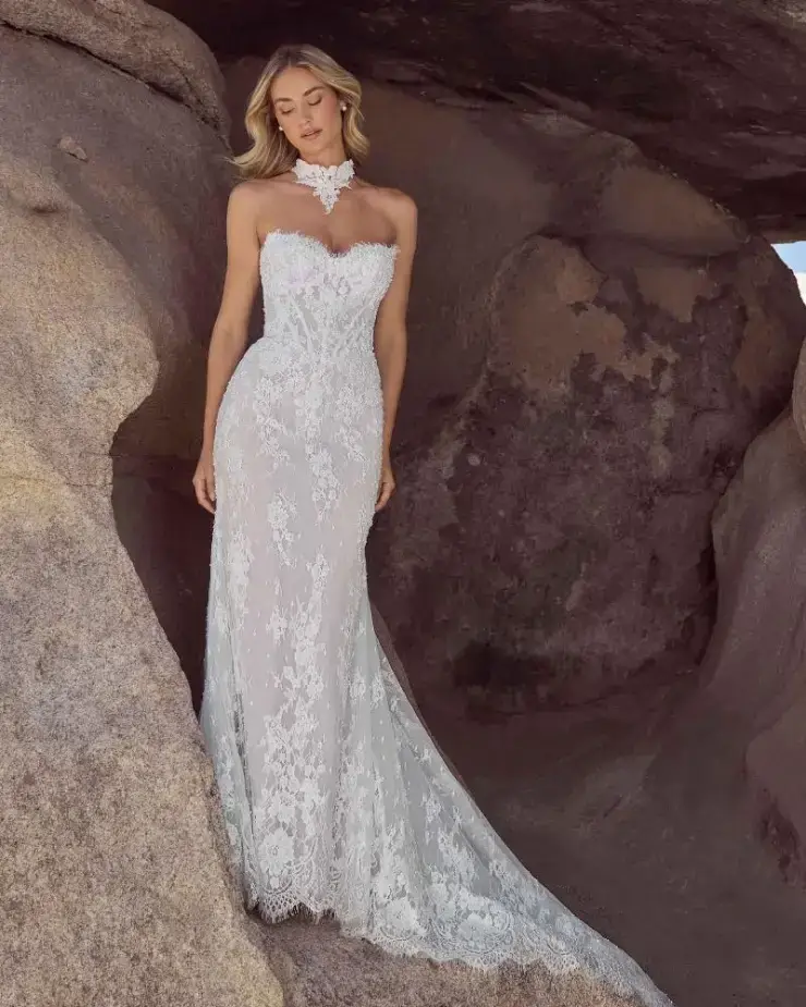 A woman in a lace wedding dress standing against a rocky backdrop.