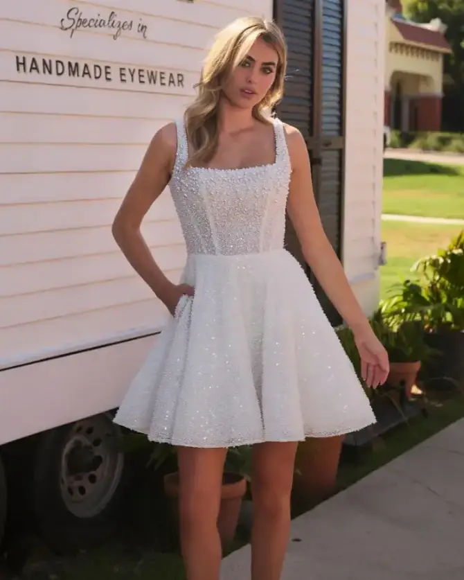 Model is wearing a short a-line bridal gown with a square neckline and pockets 