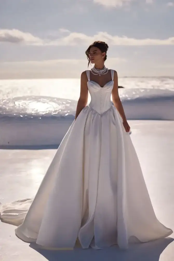 A woman wearing a stunning white gown standing on a beach with the ocean in the background.