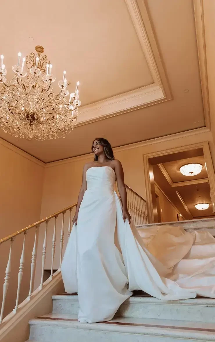 model is wearing a strapless bridal gown with an overskirt