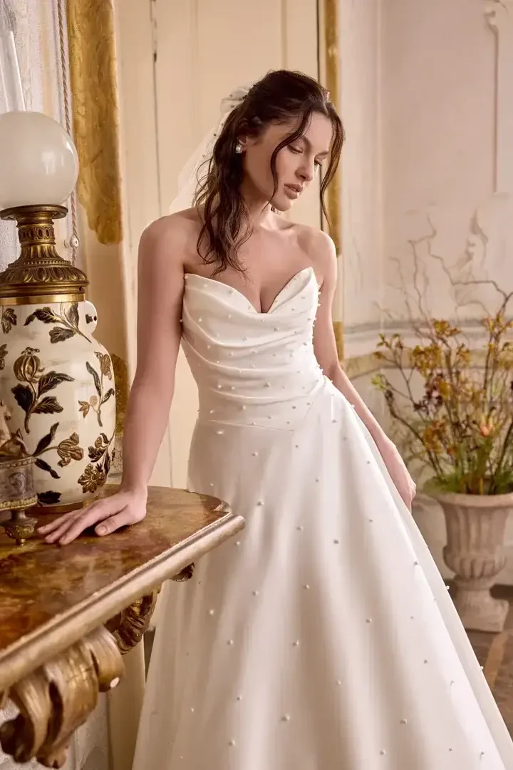model is wearing a sleeveles bridal gown with pearl accents