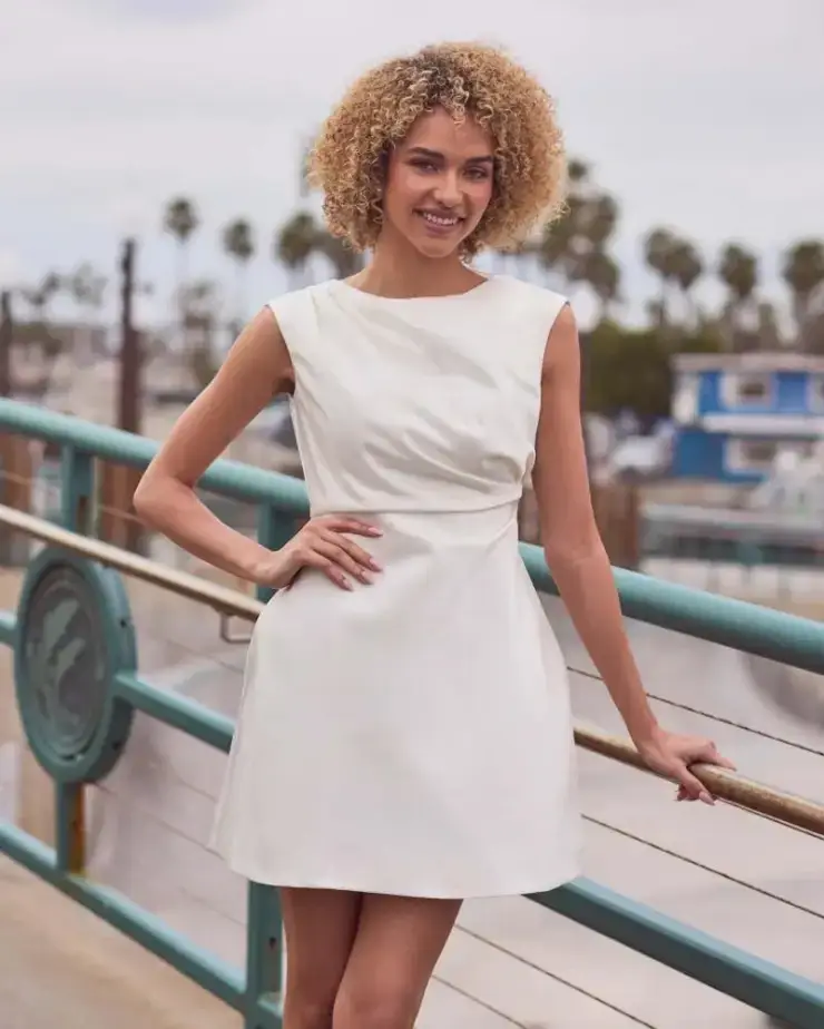 Model is wearing a short minimalist wedding dress with a high neckline and deep v back with an a-line silhouette 